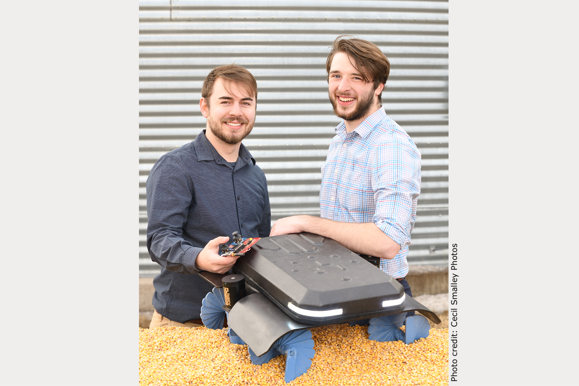 University of Nebraska Omaha undergraduate students Benjamin Johnson and Zane Zents with their Grain Weevil robot that is sitting on top of a pile of grain.